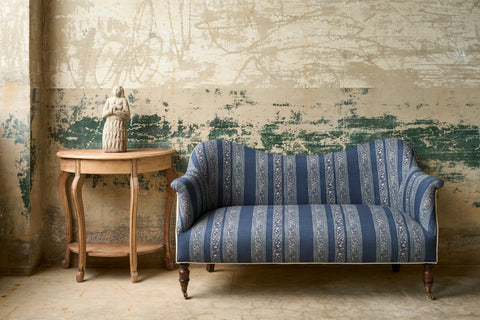 Blue and white striped small sofa with a wood table on the eft and a sculpture on top. Photographed in Grecia Marine.