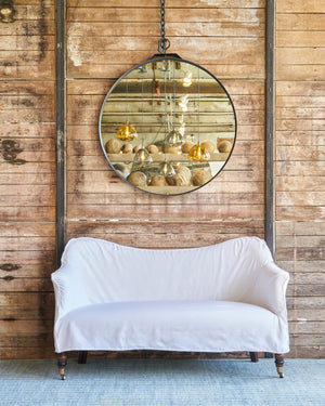  White slipcovered settee with a round mirror with a chain on a wood wall. Photographed in Otis White. 