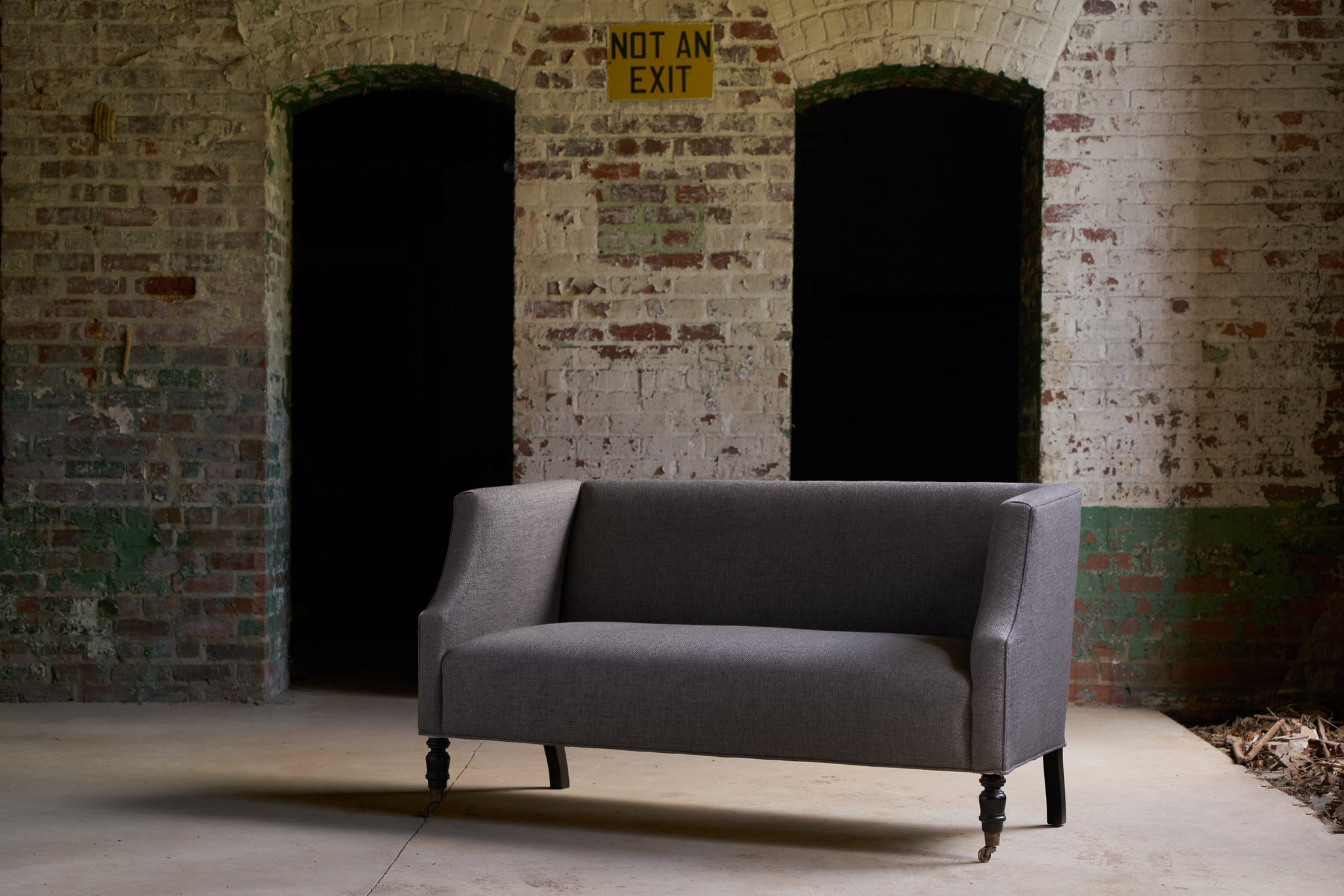  Loveseat in a warehouse in front of a white and green brick wall. Photographed in Bellamy Pewter. 