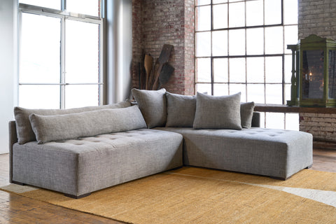 Sectional in a showroom with a yellow rug. Wood console in the background and a green wood chest. Photographed in Raven Peppercorn. 