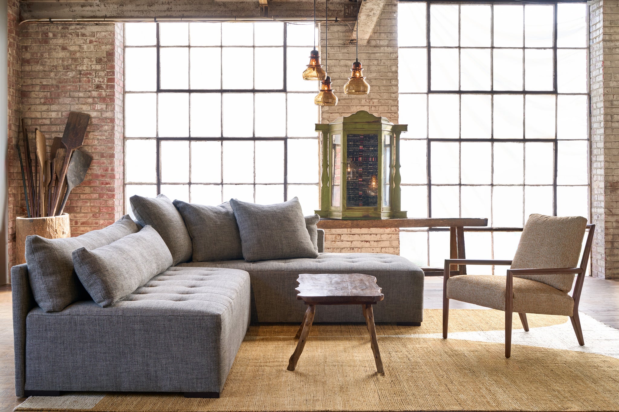  Sectional in a showroom with a yellow rug and a wood coffee table. Wood chair with an oatmeal cushion. Wood console in the background and a green wood chest. Photographed in Raven Peppercorn.  