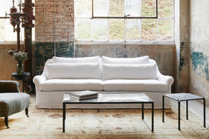  White slipcovered sofa in a showroom with a table in front. Photographed in Brevard Ivory. 