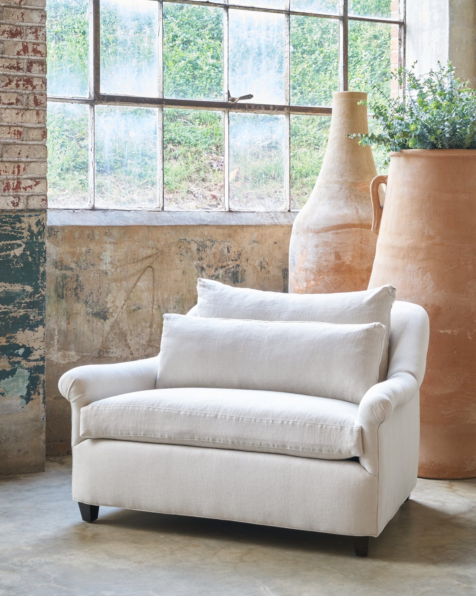  Large chair in front of a window and 2 tall terracotta pots. Photographed in Noah Bone. 