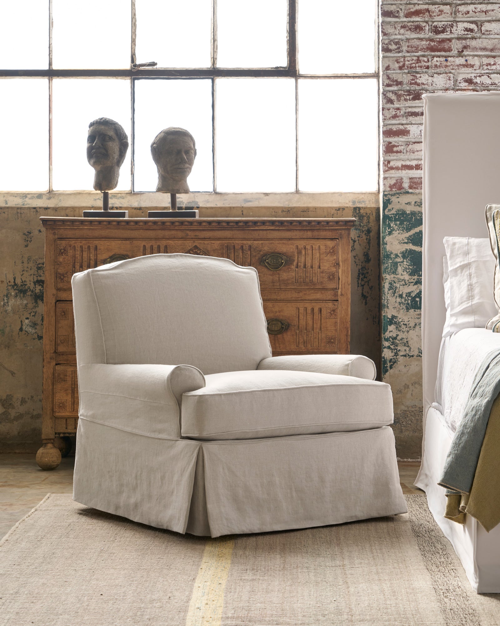  Chair by a bed with a chest of drawers behind. Photographed in Noah Bone. 