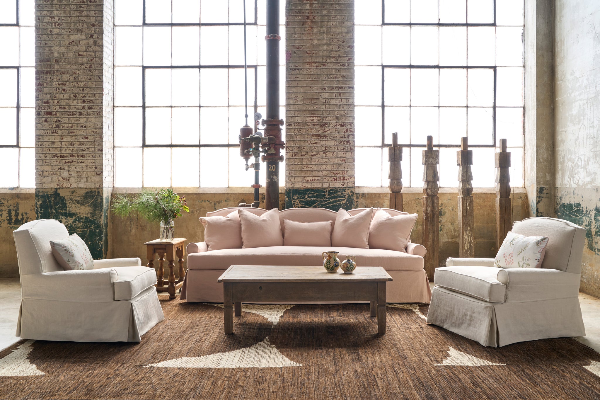  Chairs on each side of a pink sofa with wood sculptures behind. A wood coffee table in front. Photographed in Noah Bone. 