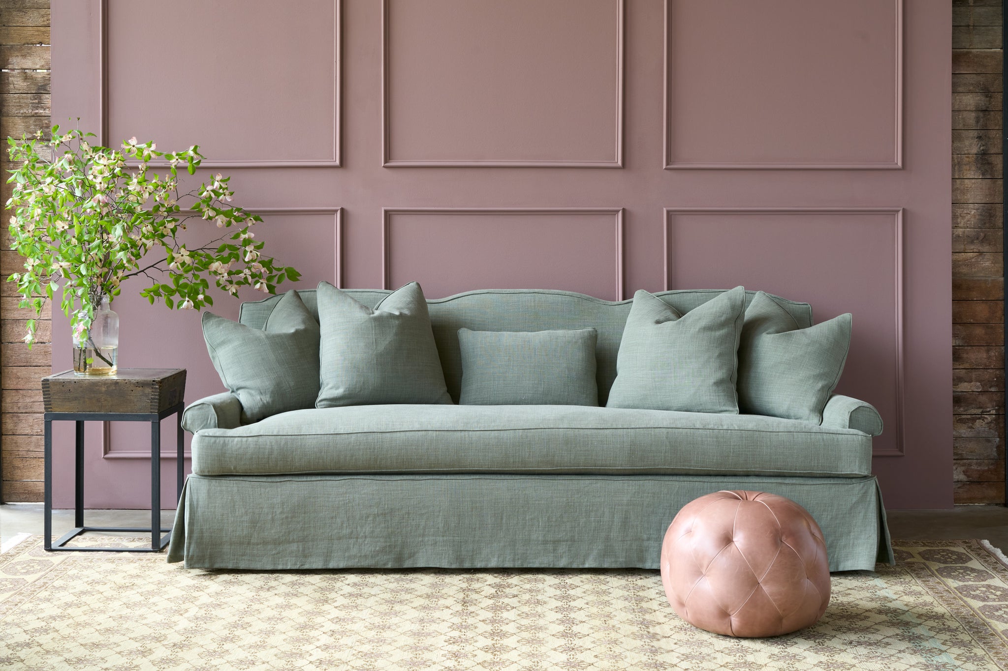  Green linen sofa in front of a purple wall with a pink leather pouf and flowers on a table on the left. Photographed in Rye Forest. 