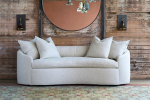  Beige sofa with decorative pillows against a wooden wall with a round mirror. Photographed in Devon Oatmeal. 