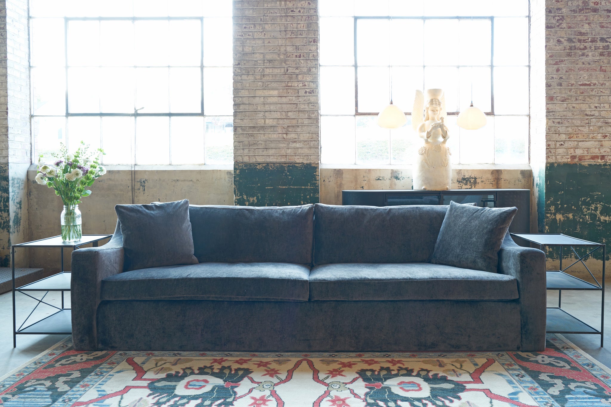  Gray sofa in a room with brick walls and large windows. Photographed in Velluto Slate. 
