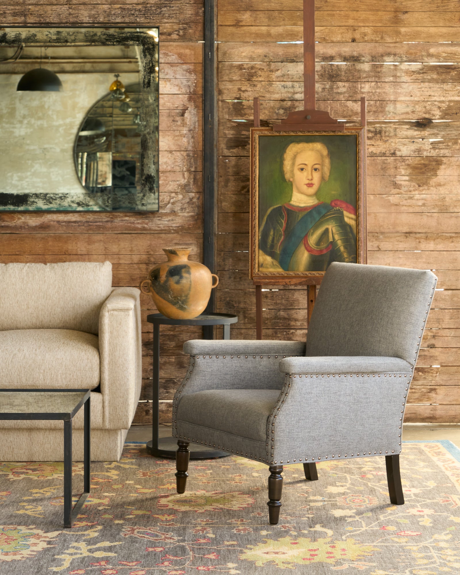  Brown chair with nailheads in front of a painting and in front of a wood wall. Photographed in Bellamy Pewter. 