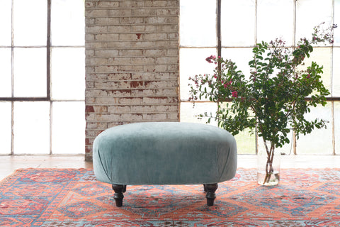 Velvet ottoman on a red vintage carpet with a vase with flowers. Photographed in Velluto Aqua.