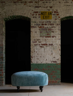  Velvet ottoman in a warehouse in front of an old white and green brick wall. Photographed in Velluto Aqua. 