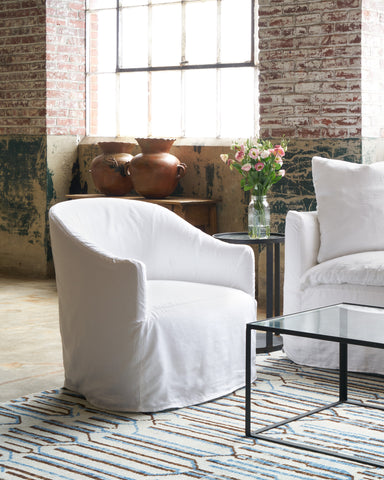 Two white chairs in a room with a brick wall and a glass coffee table. Photographed in Otis White.