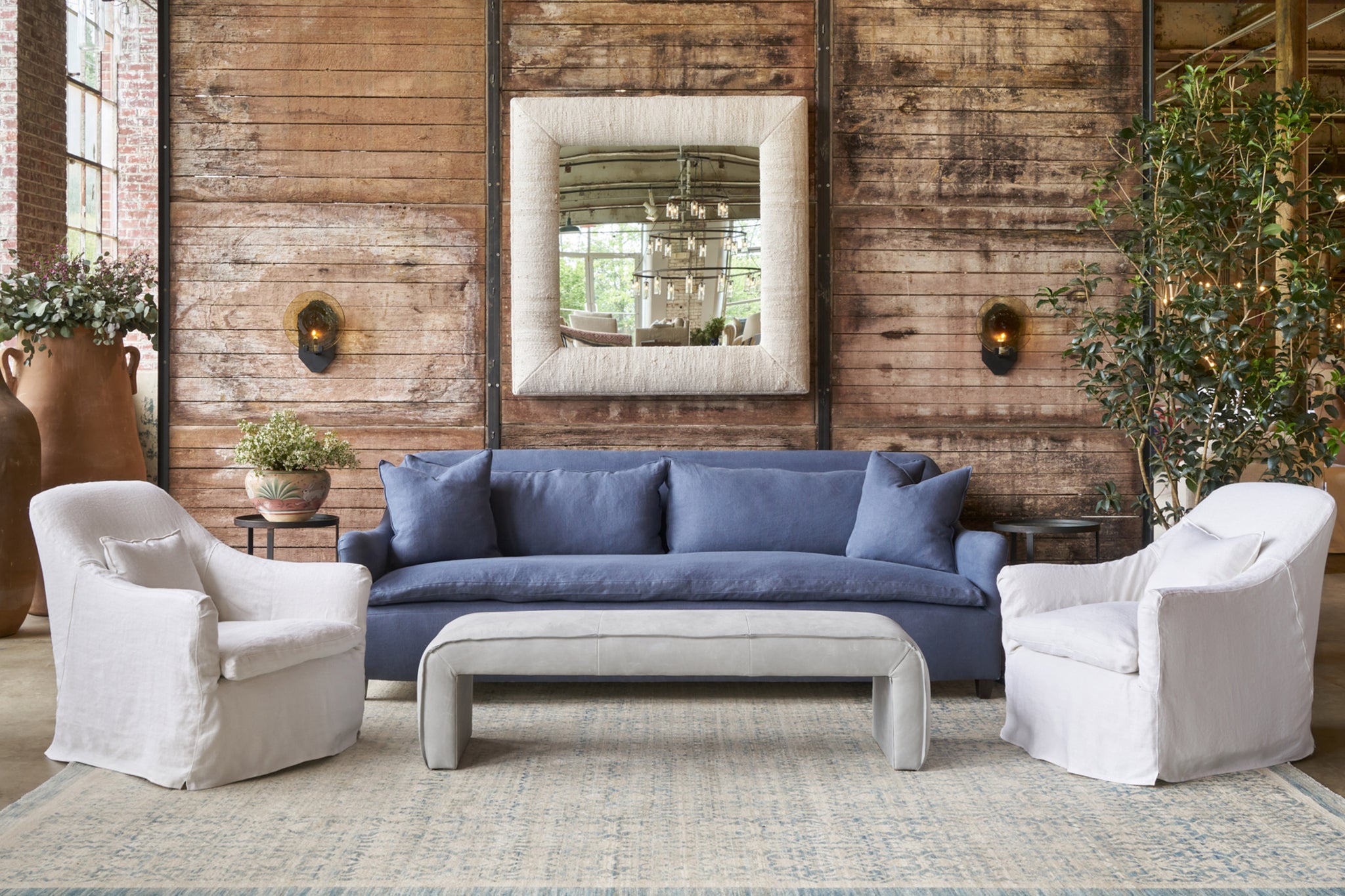  Blue sofa in front of a wood wall with 2 white chairs and a grey leather bench. Photographed in Bracco Dove. 