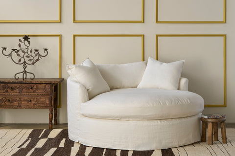 White sofa with decorative pillows in a room with gold-framed walls and a wooden side table. Photographed in Devon Ivory.
