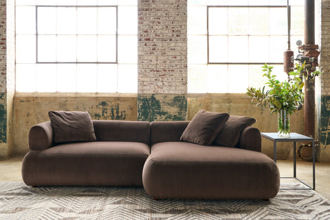 Brown sectional Sofa in a showroom in front of windows with a table on the right and a vase with greenery on the right. Photographed in Goldie Espresso.