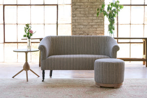  Striped sofa with a striped ottoman with a side table on the left with flowers on top. Photographed in Hickory Noire. 