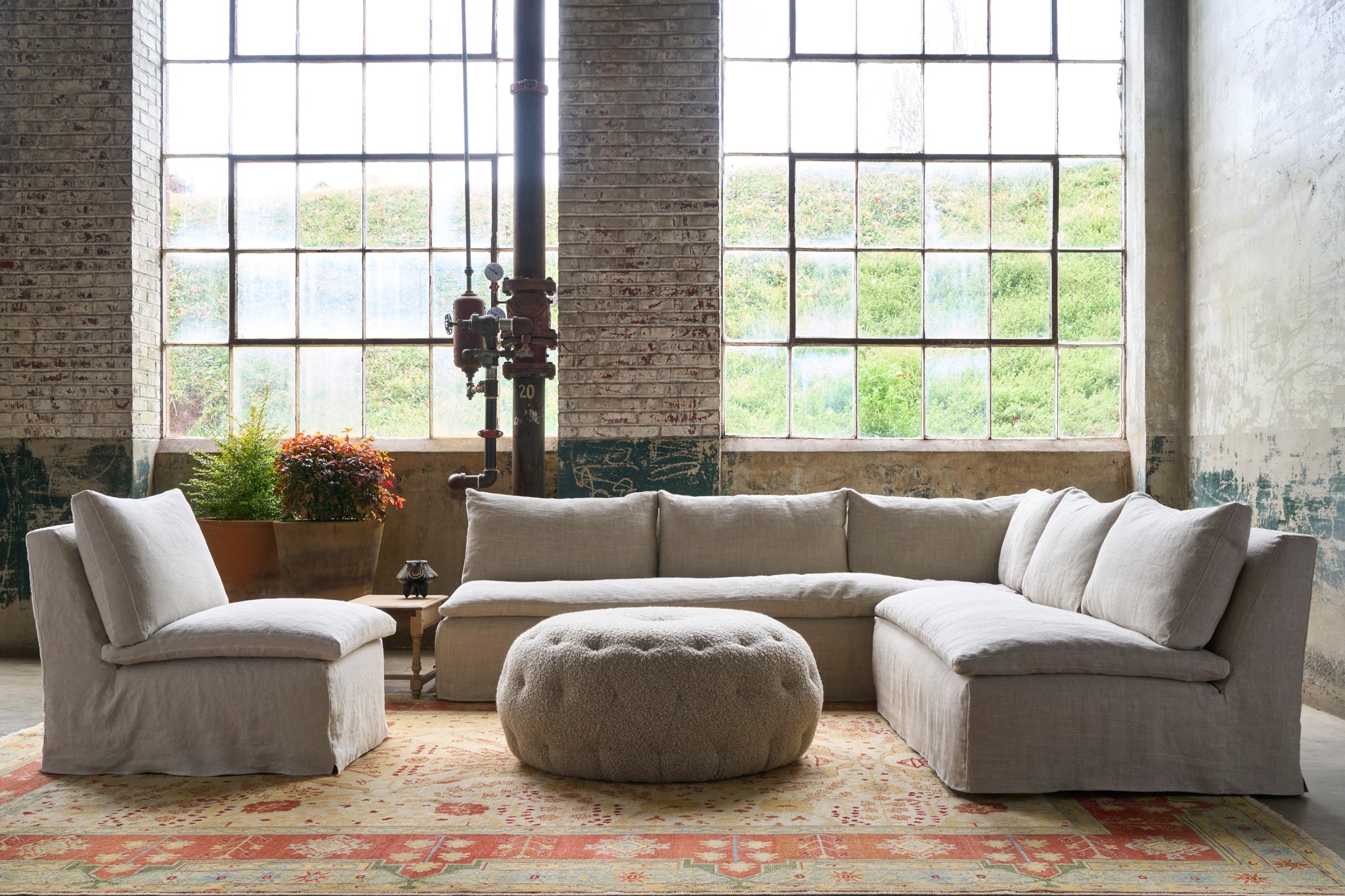  Sectional and chair in front of windows with a round tufted ottoman in the middle, on a red and yellow carpet. Photographed in Devon Oatmeal. 