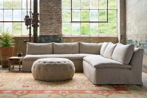 Sectional in front of windows on a red and oatmeal rug. Pouf ottoman in the middle. Photographed in Devon Oatmeal.