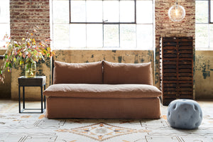  Brown armless sofa in front of  a window with a blue ottoman. Photographed in Rye Spice. 