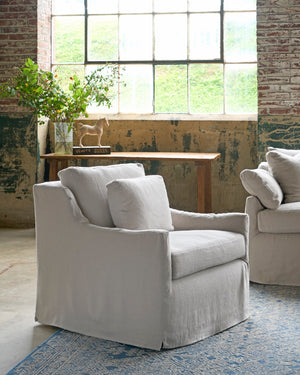  Chair next to a sofa in front of a window. A wood console behind with a bouquet and a small horse sculpture. Photographed in Brevard Mist. 