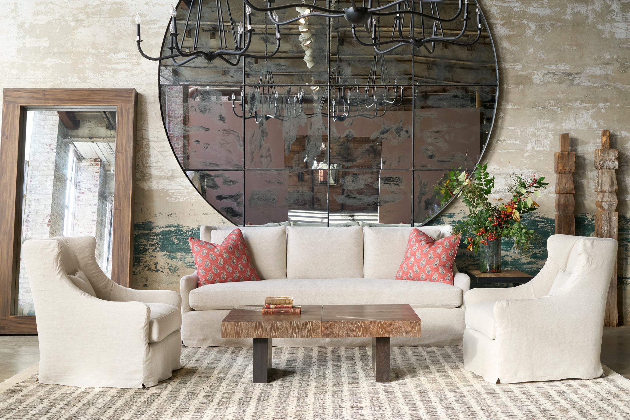  Living room with beige sofa, armchairs, and a large round mirror on the wall. Photographed in Olvera Oatmeal. 