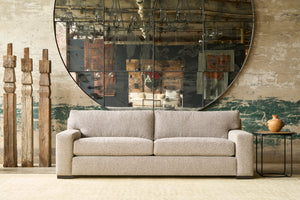  Grey sofa in front of a large mirror. 3 wood sculptures on the left with a plant. Photographed in Bonn Birch. 