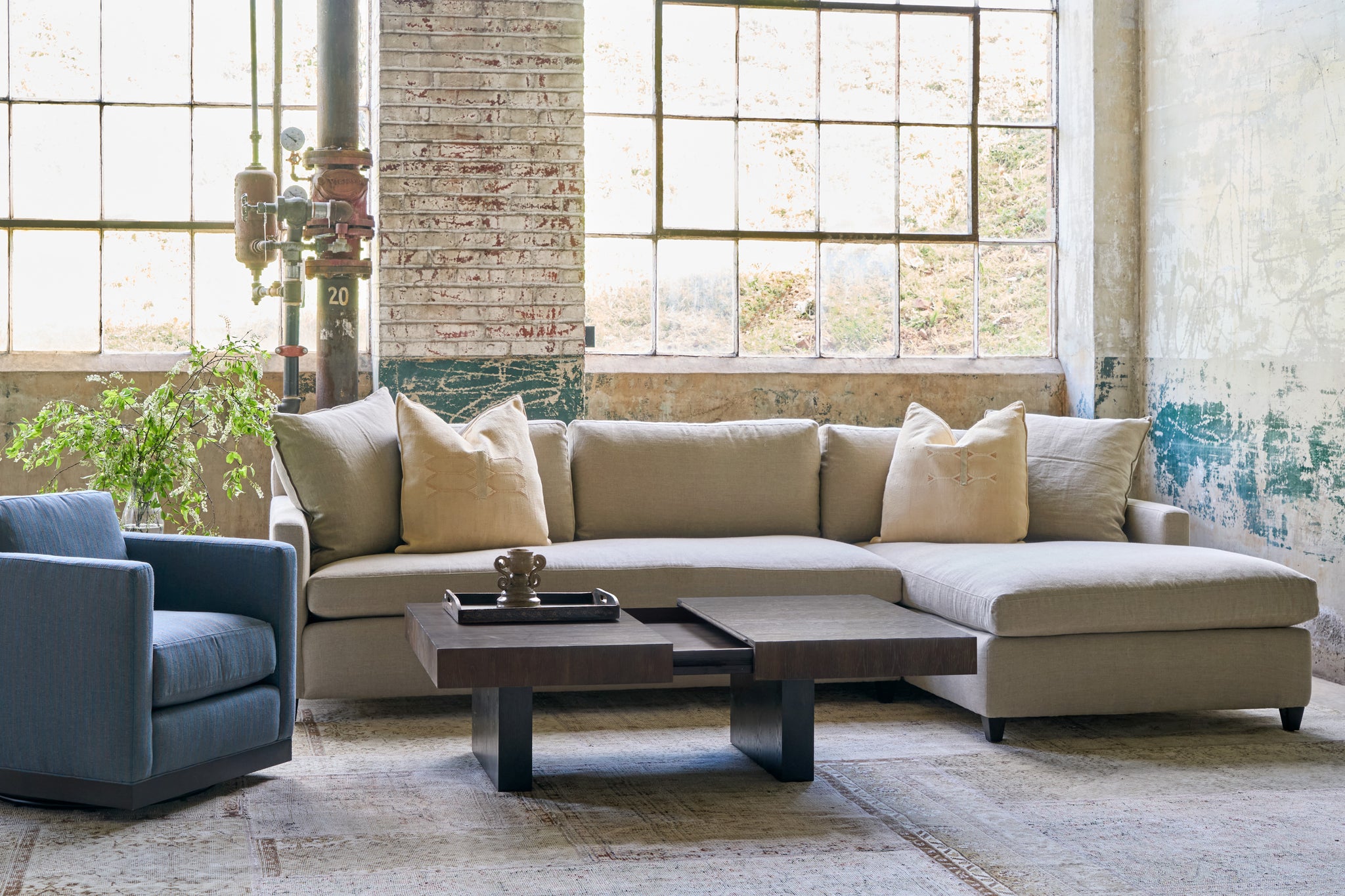  Sectional sofa in an oatmeal color with a Cosmo Mini Chair on the left side. A coffee table in wood that expands is in front. Photographed in Ashville Burlap. 