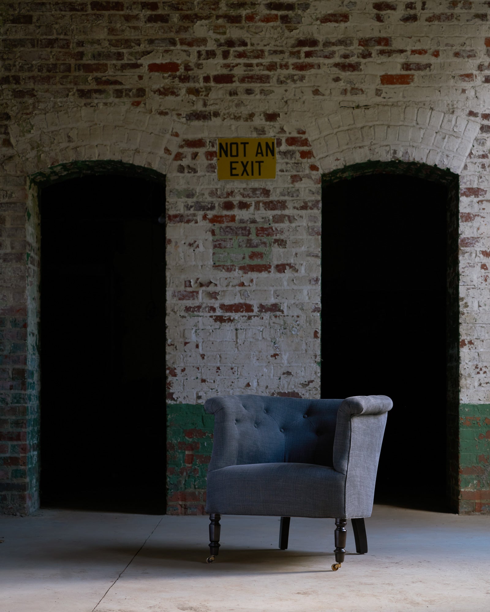  Chair in a grey linen in a warehouse in front of an old brick wall. Photographed in Rye Black. 