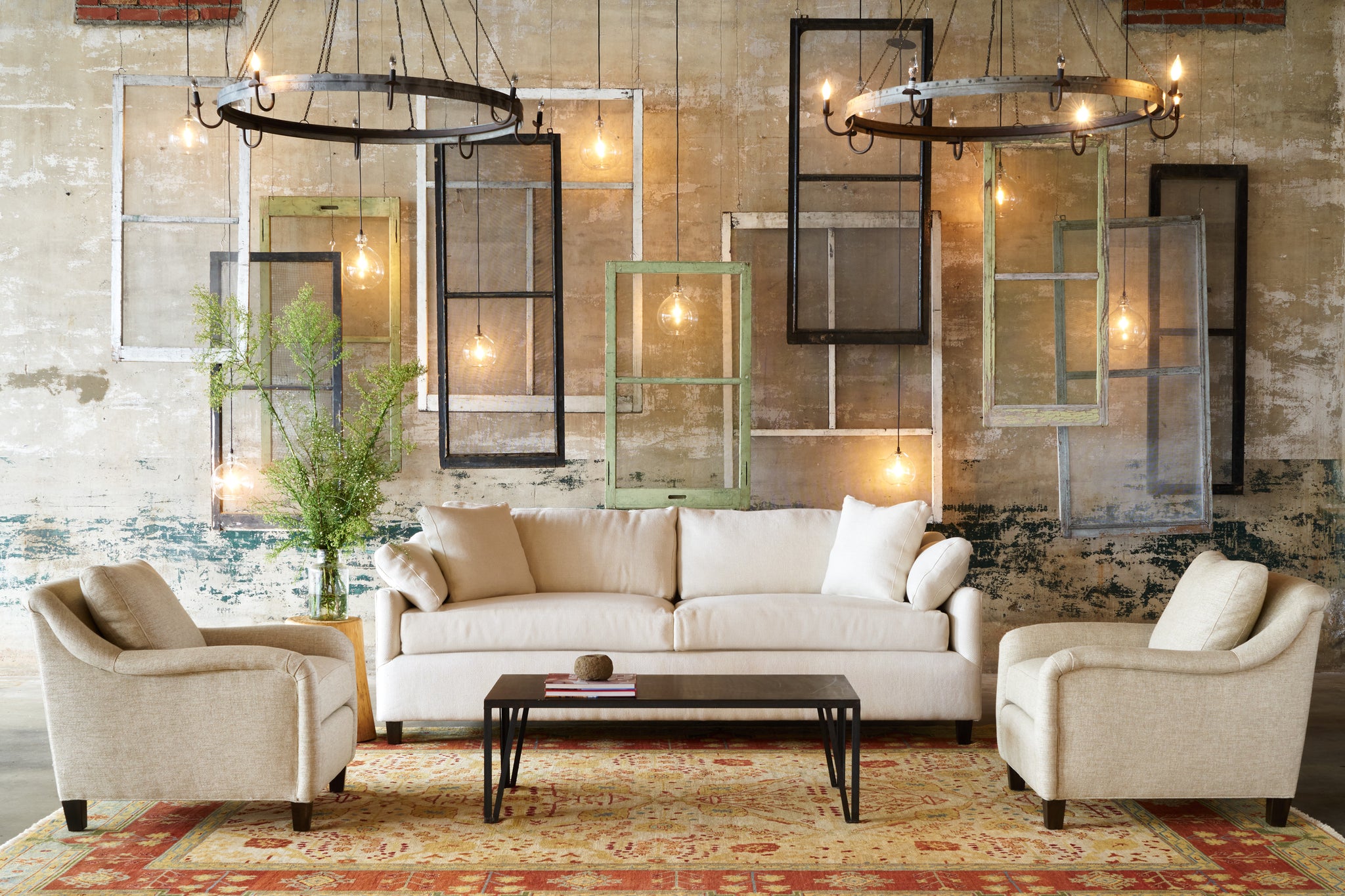  White sofa with a chair on each side in front of a wall with vintage window panes and lights. Black coffee table in front. Photographed in Bellamy Oatmeal. 