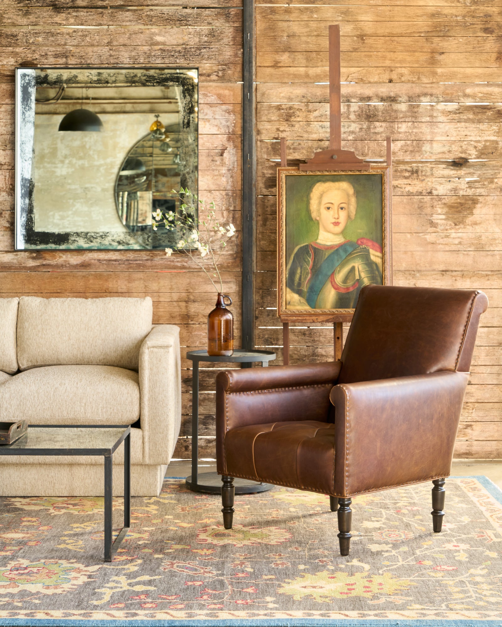  Brown leather chair by a sofa in front of a mirror and a painting of a woman on an easel. Photographed in Spur Chocolate. 