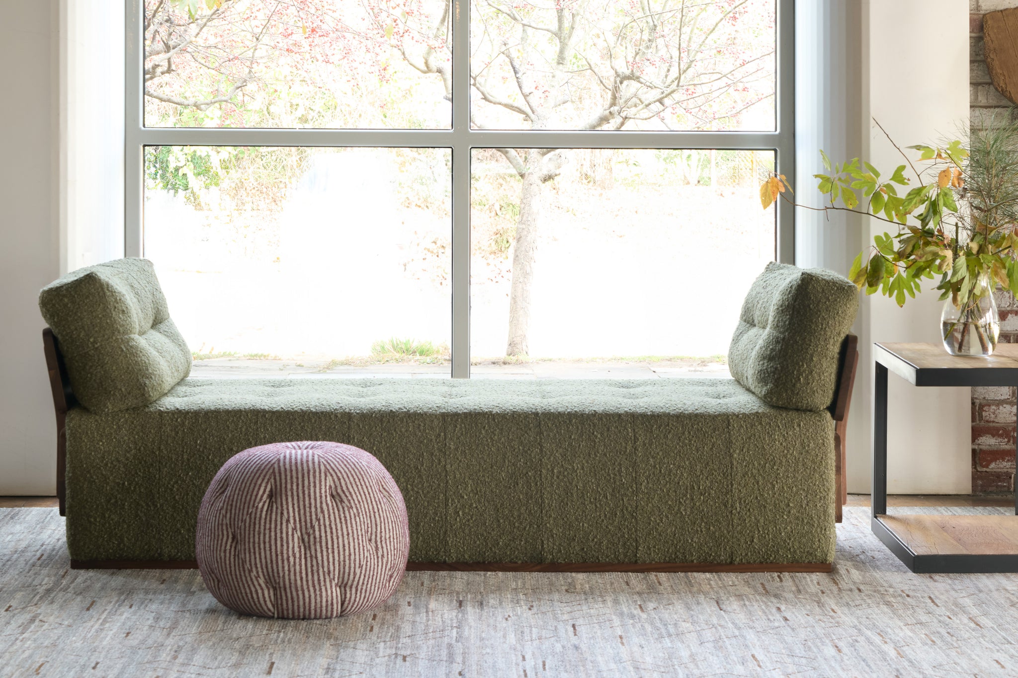  Green upholstered bench with a pink pouf in a room with large windows. Photographed in Shiloh Plum. 