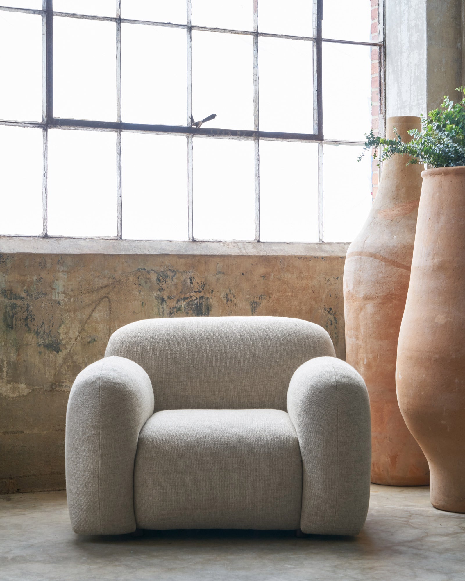  Chair in a showroom in front of a large window next to 2 tall terracotta pots. Photographed in Bellamy Oatmeal. 