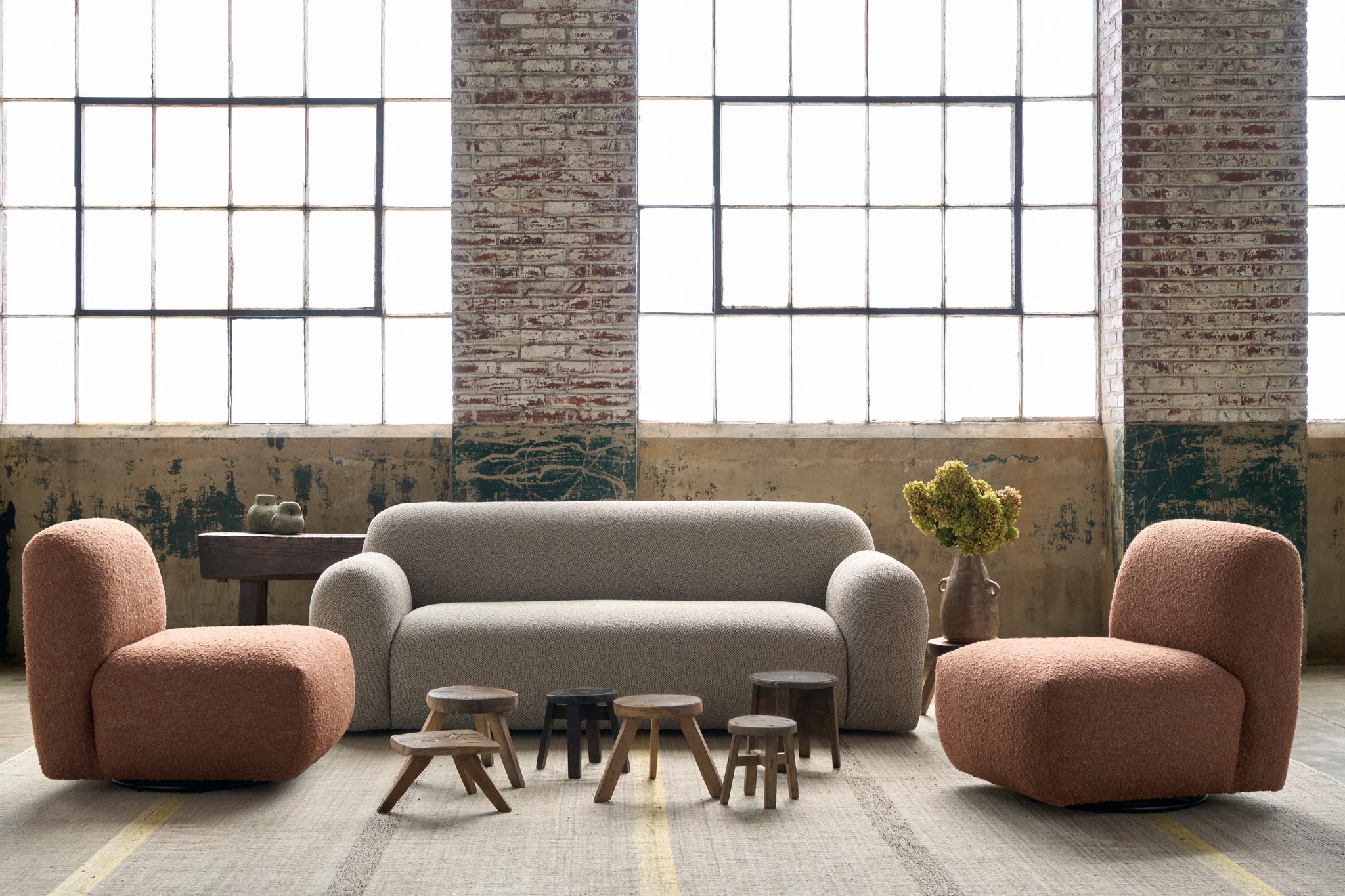  Sofa and 2 armless chairs in a showroom in front of large windows. There are 6 mini wood stools in front. Flowers on the right side of the sofa. Photographed in Bonn Birch. 