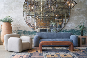  Grey sofa in front of a large mirror. Natural color chair on the left and a brown leather bench in front. Photographed in Bruges Indigo. 