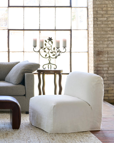 White armchair in a living room with a large window and brick wall. Photographed in Olvera Ivory.