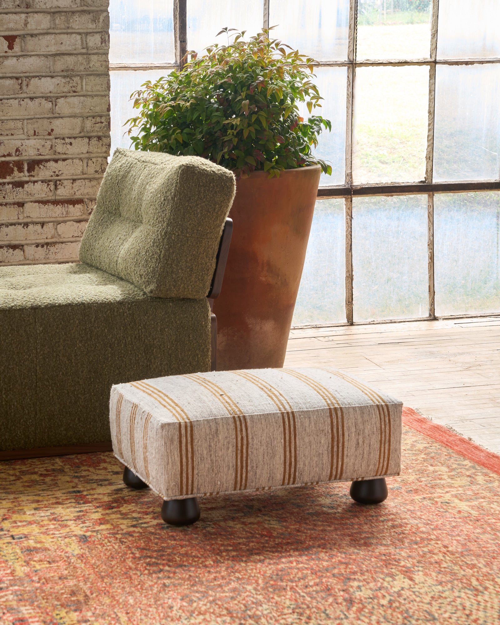  Striped ottoman in front of a green sofa with a large plant in the background. Photographed in Vintage Hemp. 