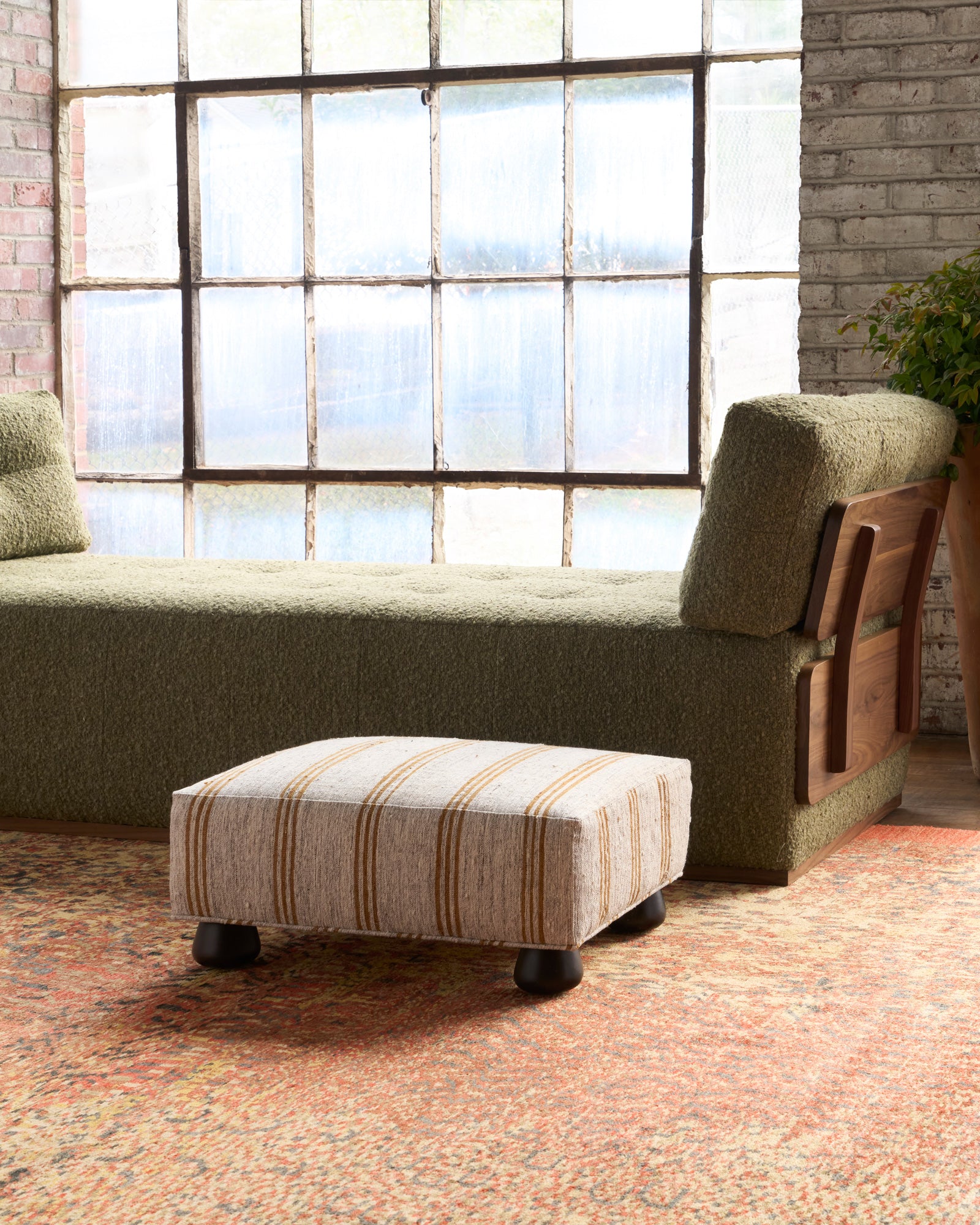  Sofa with striped ottoman in a room with large windows and brick walls. Photographed in Vintage Hemp. 