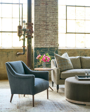  Black chair next ro a sofa with a side table with pink flowers on a table. Velvet ottoman with a wood base in front with a tray and 2 glasses. Photographed in Rye Black. 