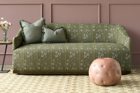 Pink leather pouf in front of a green sofa. Photographed in Solvang Mauve.