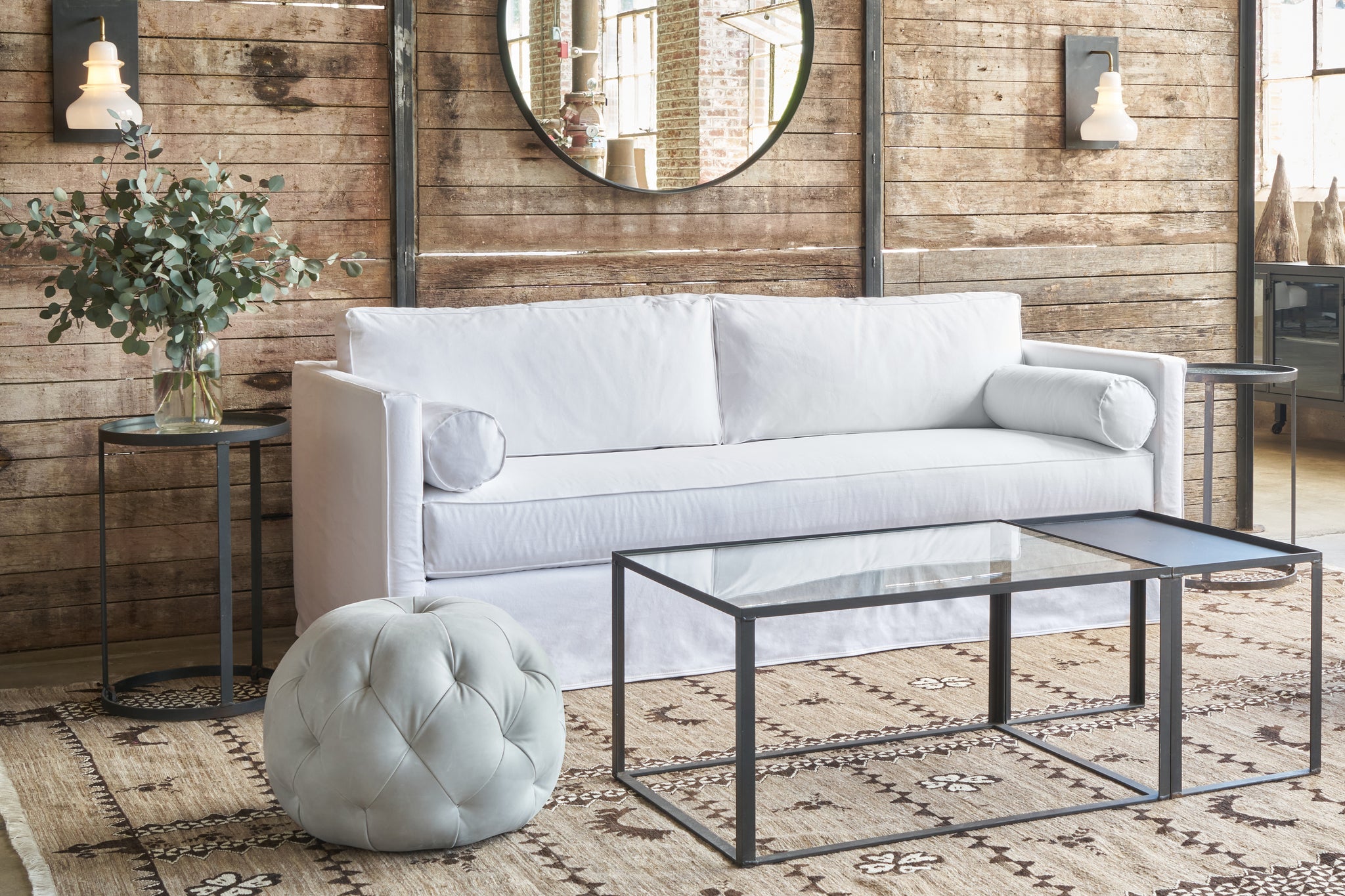  White sofa in front of a wood wall with a pouf in grey leather. Photographed in Bracco Dove. 
