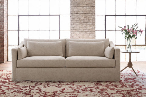 Beige sofa in a room with large windows and a brick wall. Photographed in Bellamy Natural.