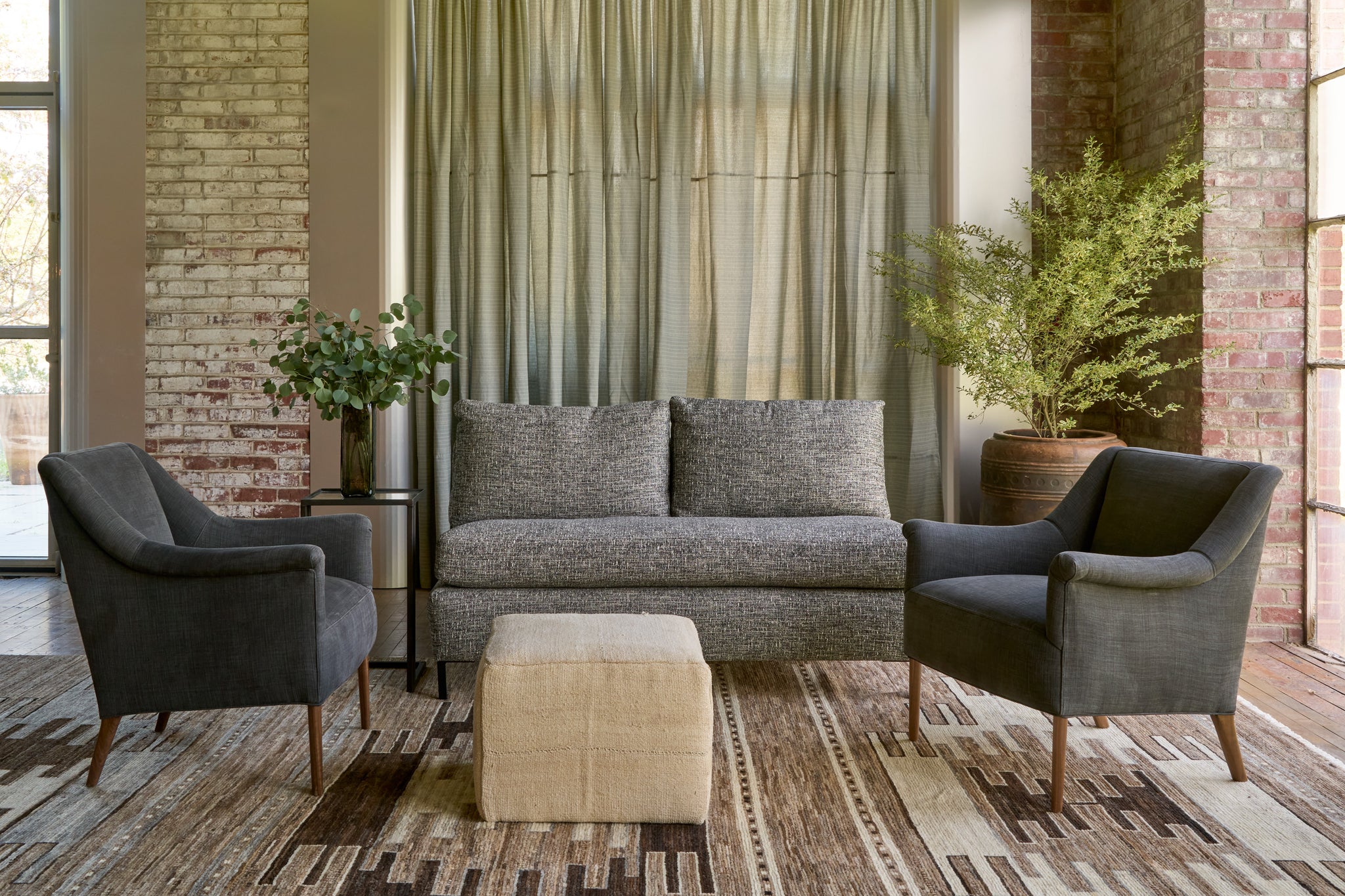  Arless sofa with 2 black chairs and a cream colored cube in front. Grey curtain in the back and tree in a pot in the right corner. Photographed in Verona Black. 