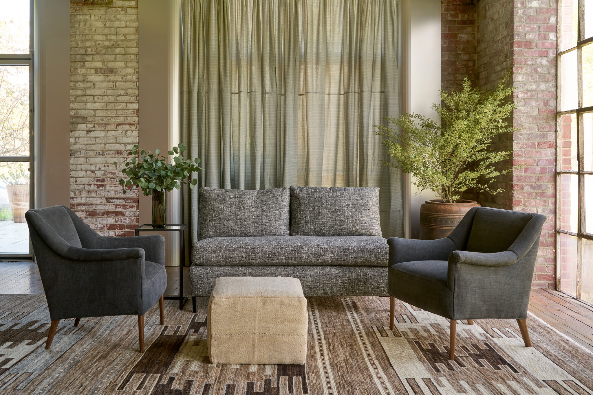  Armless loveseat with 2 black chairs and a cream ottoman. Curtains in the back. Photographed in Rye Black. 