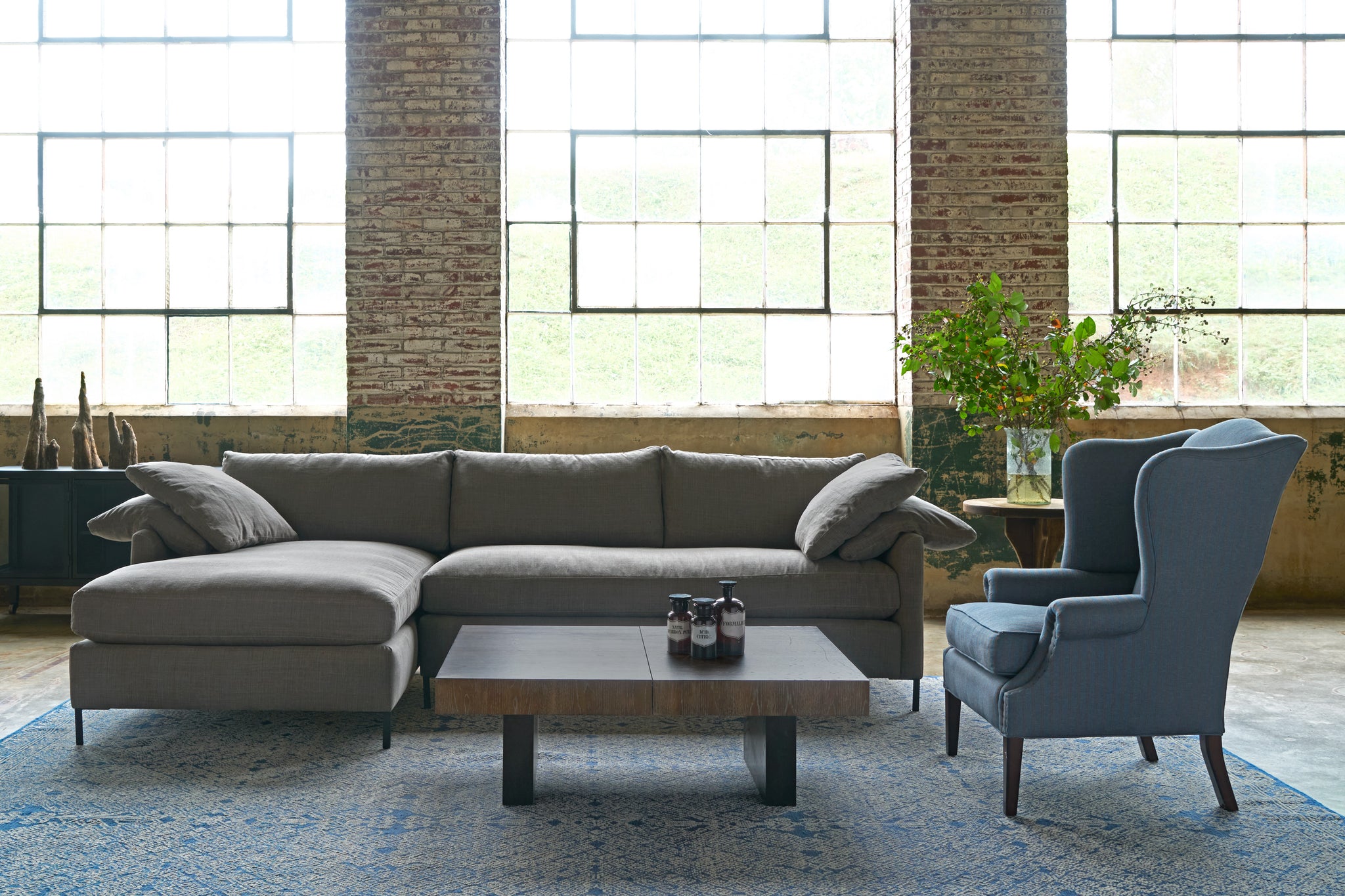  Sectional sofa in dark grey linen with a wing chair on the right and a wood coffee table. Photographed in Rye Warm Grey. 