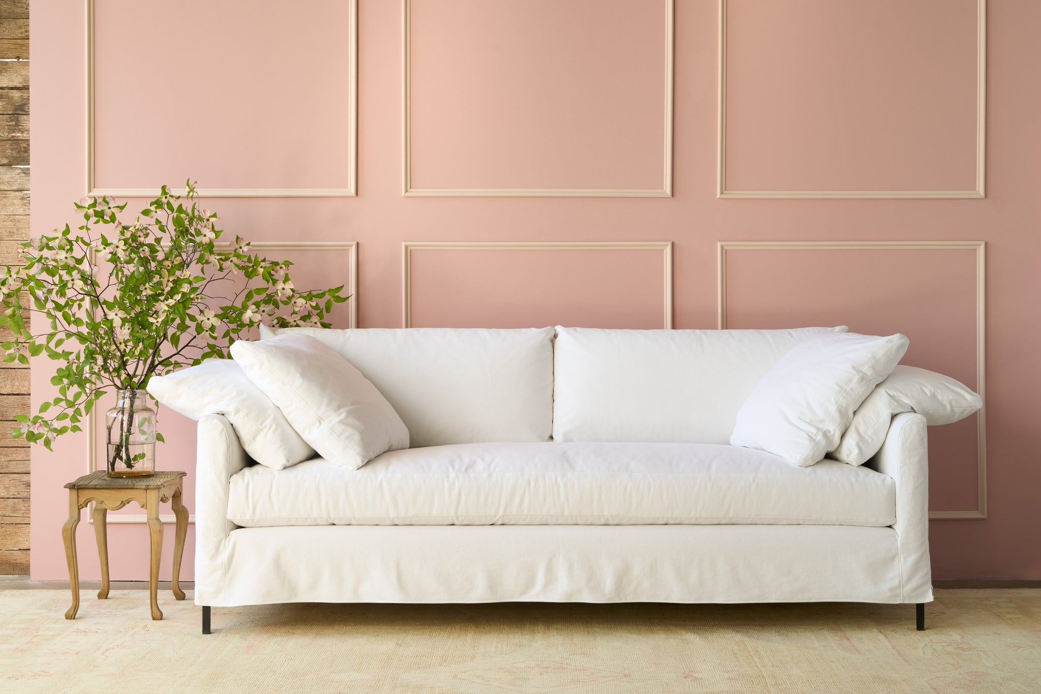  Slipcovered white sofa in front of a pink wall with a large bouquet on the left on top of a wood table. Photographed in Denim White. 