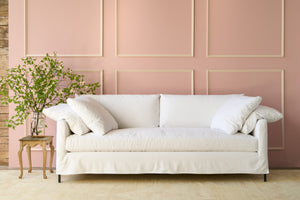  Slipcovered white sofa in front of a pink wall with a large bouquet on the left on top of a wood table. Photographed in Denim White. 