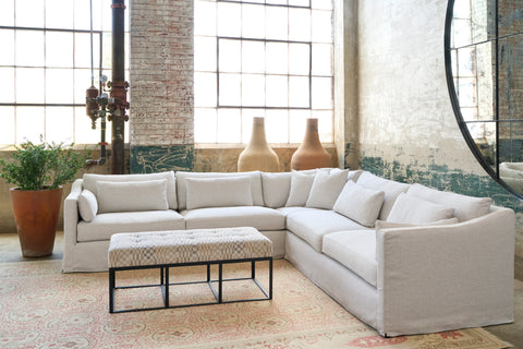 White sectional in a room with a checkered ottoman in front and a terracotta pot with a plant. Photographed in Sandy Natural.