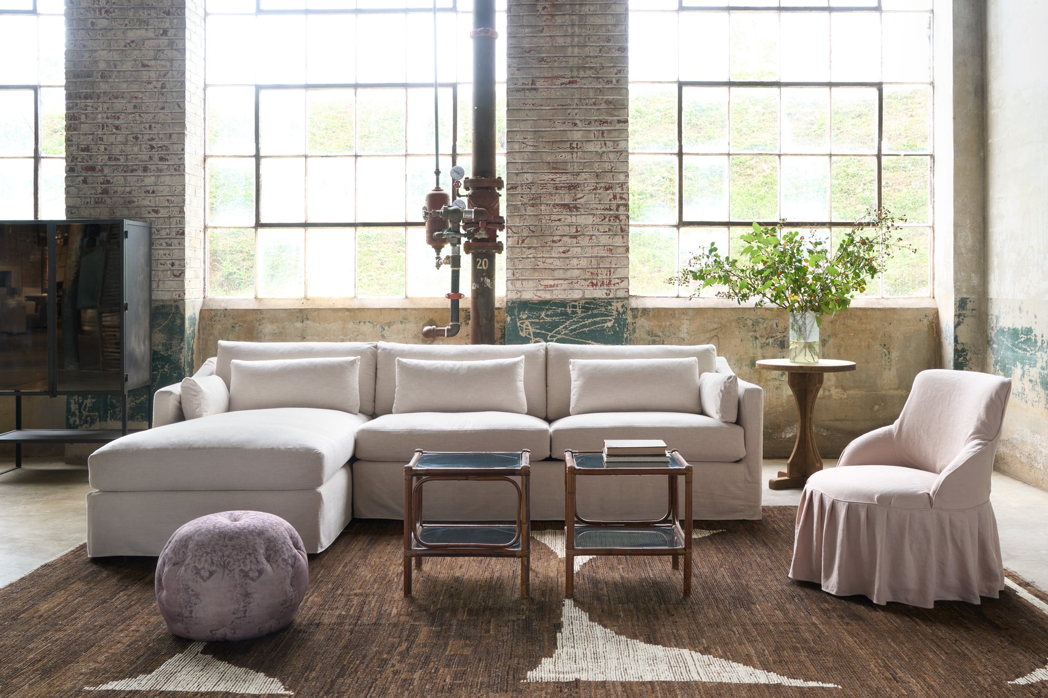  Sectional sofa in cream fabric with a pink chair on the right, 2 small table in front and a pouf on the brown rug. Photographed in Chevron Cream. 