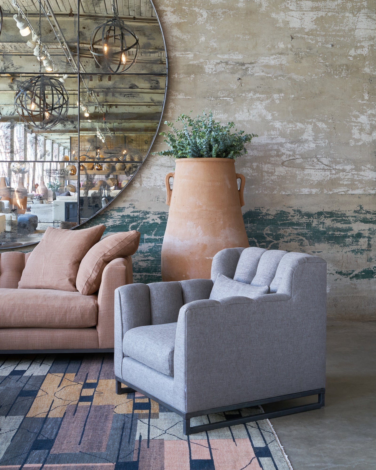  Grey chair in front of a concrete wall with an oversized mirror and a brown sofa and tall terracotta pot. Photographed in Bellamy Pewter. 