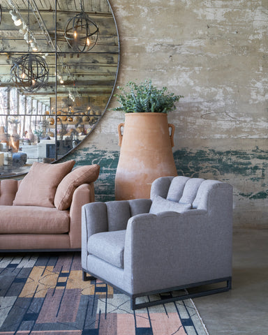 Grey chair in front of a concrete wall with an oversized mirror and a brown sofa and tall terracotta pot. Photographed in Bellamy Pewter.